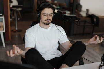 A man in casual clothing meditates with headphones on in a modern living room, finding inner peace and relaxation.