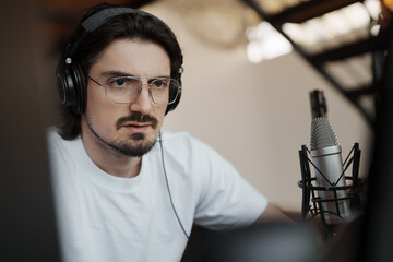 Man wearing headphones and speaking into a microphone while recording a podcast. He looks focused and engaged in a studio setting.