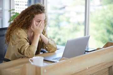 young woman working on laptop computer and feeling tired and worry from hard work in the office