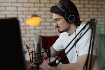 A man in a white shirt and headphones recording a podcast in a home studio with professional equipment. He is focused and engaged in his work.