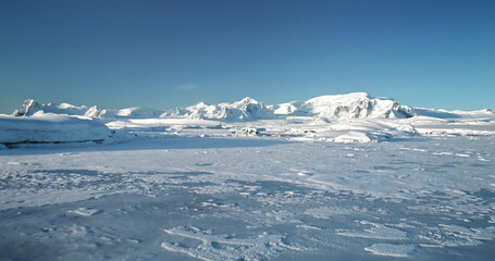 Fly over snowy mountain landscape in Antarctica. Polar frozen ocean landscape covered by snow under...