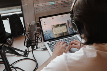 Close-up of an individual using a laptop for audio production, with a professional microphone and headphones.