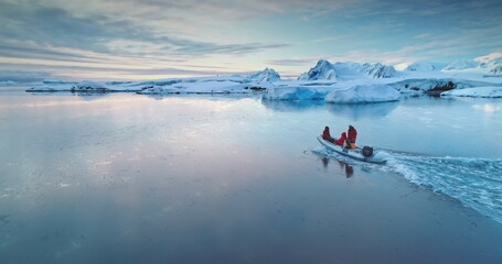 Tourists people sail on boat in Antarctica. Zodiac boat gently glides on waters surface in sunset...
