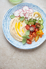 Blue and white plate with hummus and fresh veggies on a beige stone background, vertical shot with space, flat lay