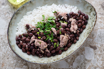 Bowl of black beans with chicken meat and white rice, horizontal shot on a light-brown granite background