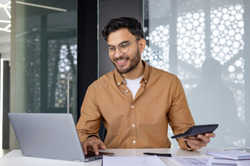 Financier auditing paperwork using calculator and laptop in modern office