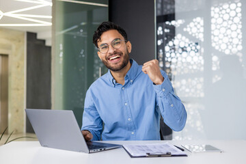 Happy professional celebrating success at work with laptop in modern office