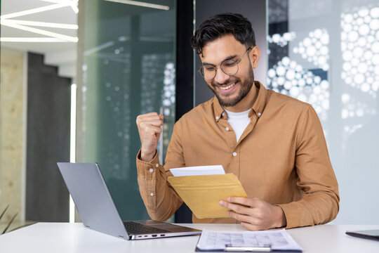 Excited young professional rejoices while reading letter at work desk