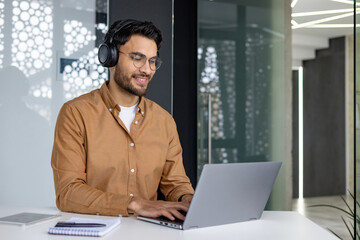 Smiling man in headphones working on laptop in modern office