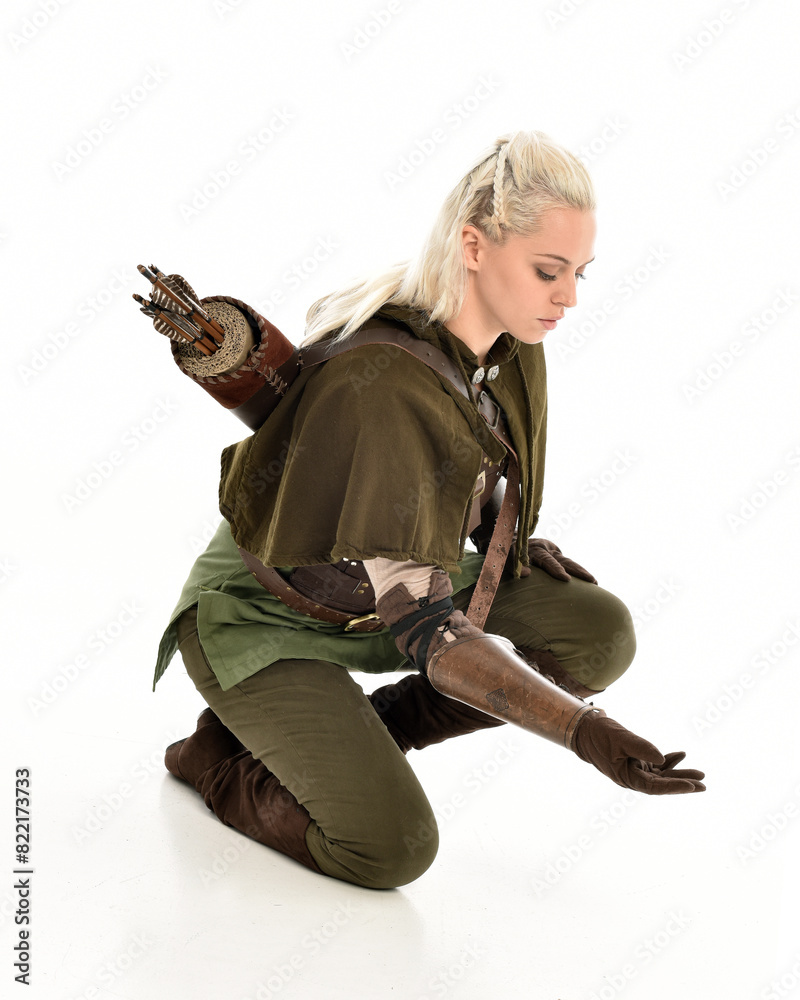 Sticker full length portrait of blonde female model wearing green fantasy elf warrior halloween costume with leather armour. sitting pose kneeling. isolated on white studio background.