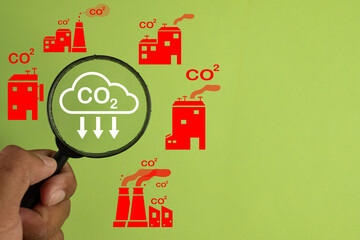 Magnifying Glass on Reduce CO2 Icon among Factory Icons for Climate Change Awareness,reducing emissions,environmental protection,pollution control, and sustainable industrial practices.