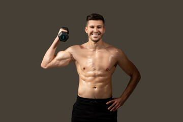 A man is standing and posing while holding a dumbbell in his hand. He is showcasing his muscles and...