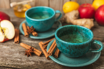 Fragrant hot tea with cinnamon stick and anise on a textured wooden background. A cup of hot tea with honey, lemon, mint and apples. Spicy tea with spices. Immunity tea. Health concept.Copy space.