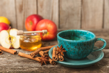 Fragrant hot tea with cinnamon stick and anise on a textured wooden background. A cup of hot tea with honey, lemon, mint and apples. Spicy tea with spices. Immunity tea. Health concept.Copy space.