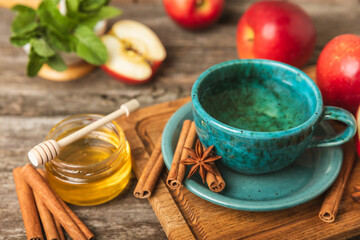 Fragrant hot tea with cinnamon stick and anise on a textured wooden background. A cup of hot tea with honey, lemon, mint and apples. Spicy tea with spices. Immunity tea. Health concept.Copy space.