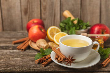 Fragrant hot tea with cinnamon stick and anise on a textured wooden background. A cup of hot tea with honey, lemon, mint and apples. Spicy tea with spices. Immunity tea. Health concept.Copy space.