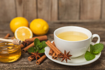 Fragrant hot tea with cinnamon stick and anise on a textured wooden background. A cup of hot tea with honey, lemon, mint and apples. Spicy tea with spices. Immunity tea. Health concept.Copy space.