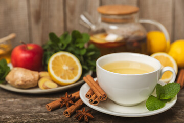 Fragrant hot tea with cinnamon stick and anise on a textured wooden background. A cup of hot tea with honey, lemon, mint and apples. Spicy tea with spices. Immunity tea. Health concept.Copy space.