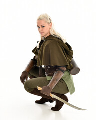Fototapeta premium full length portrait of blonde female model wearing green fantasy elf warrior halloween costume with leather armour. sitting pose kneeling. isolated on white studio background.