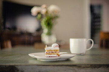 An isolated piece of cake on a plate with a fork, a cup, and flowers in the background.