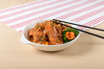A bowl of Prawn with chopsticks on a table. The food is a mix of meat and vegetables, and the chopsticks are placed on top of the food