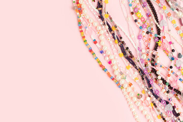 Colorful chains of beads, pearls and natural stones on a pink background. Composition with copy space.