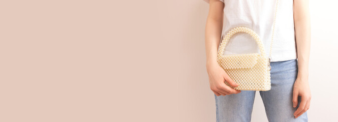 Woman with a beaded pearl handbag over her shoulder in front of beige background.   Banner with...