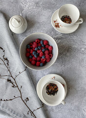 White cups and bowl with berries on a gray background