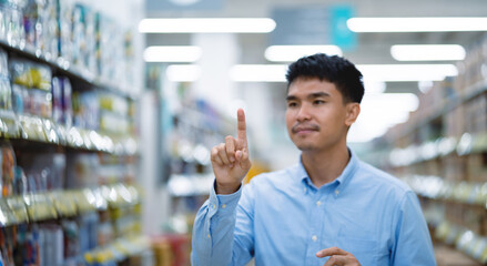 A man in a blue shirt is pointing at a product in a store. He is using his finger to indicate that...