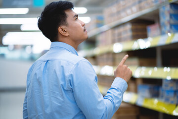 A man in a blue shirt is pointing at a shelf in a store. He is looking at the items on the shelf...