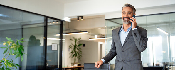 Banner middle aged Latin or Indian businessman having call on smartphone with business partners or...