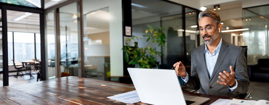 Middle age hispanic man using computer remote for business studying, watching online virtual webinar training meeting, video call. Mature businessman talking on laptop in office. Banner, copy space