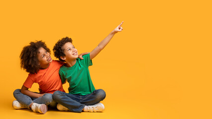 Two African American children, a boy and a girl, are sitting on a bright yellow background. They...