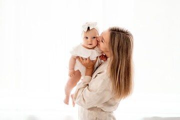a mother with a newborn baby in her arms at home on a white background of a bed or window, a space...