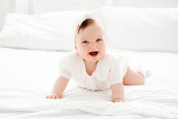 happy smiling newborn baby girl in white clothes on the bed at home, cute baby crawling, space for...