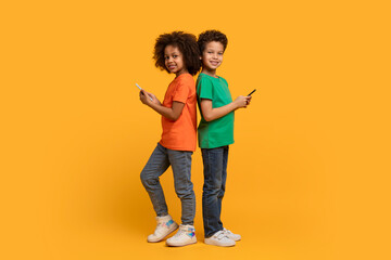 Two African American children, both holding cell phones, are shown against a vibrant yellow background. They appear engaged with their devices, their attention absorbed by the screens.