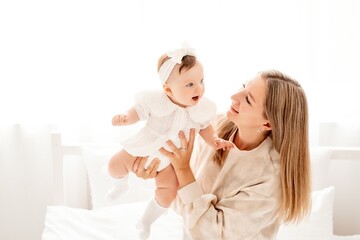 a mother with a newborn baby in her arms at home on a white background of a bed or window, a space for text, a young mother gently kisses and hugs her baby, maternal love