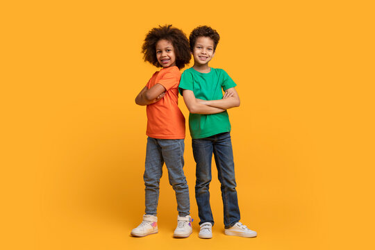 Two African American children, a boy and a girl, are standing confidently back to back with arms crossed on chest in front of a bright yellow background. - Powered by Adobe