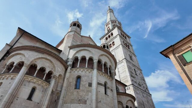 Panoramic view of the historical Modena cathedral and its iconic Ghirlandina tower under clear blue skies in downtown Modena, Italy