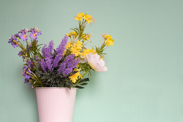 Bouquet de fleurs mauve et jaune dans un pot en ferraille beige sur fond coloré