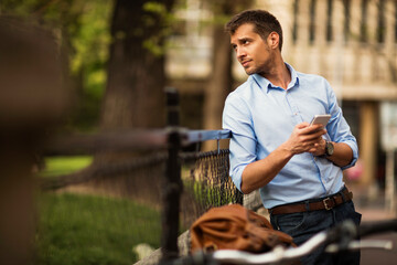 Businessman standing near a park fence with a phone in hand looking to the side