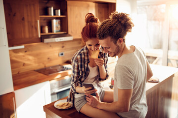 Couple enjoying breakfast in kitchen while looking at phone