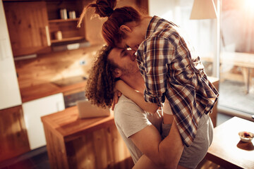 Happy couple embracing and kissing in sunny kitchen