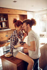Couple enjoying breakfast in kitchen while looking at phone