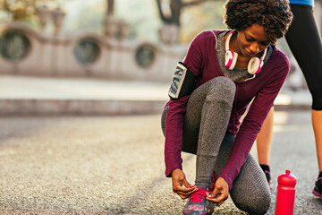 Young African American woman tying shoe laces before running in city park