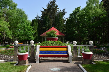 multi-colored bench against the backdrop of a flower bed and gazebo in a park in spring