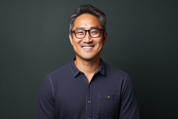 Obraz premium Portrait of a glad asian man in his 40s smiling at the camera on blank studio backdrop