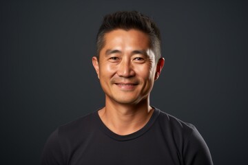 Fototapeta premium Portrait of a glad asian man in his 40s smiling at the camera on blank studio backdrop