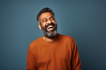 Portrait of a tender indian man in his 40s laughing in front of blank studio backdrop