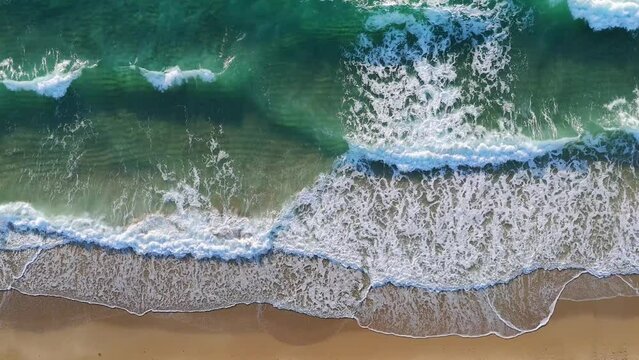 Drone view of Palm beach where ocean meeting sand. Waves breaking on shore and creating white foam. Darker shade of blue to light indicating on depths of water